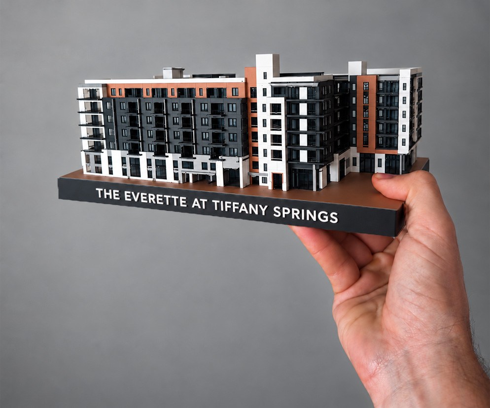 3D-printed multi-color scale model of a 7-story mixed-use apartment complex on an engraved base, held in one hand